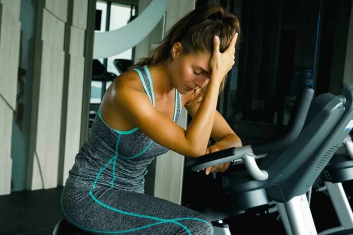 shutterstock_712430377 Woman resting on exercise bike with hand on forehead