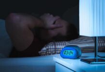 Man lying awake in bed at night beside a glowing digital alarm clock