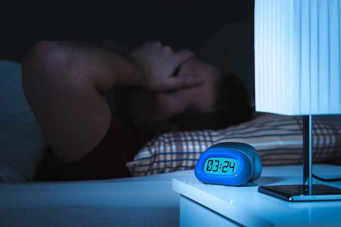 shutterstock_756899950 Man lying awake in bed at night beside a glowing digital alarm clock